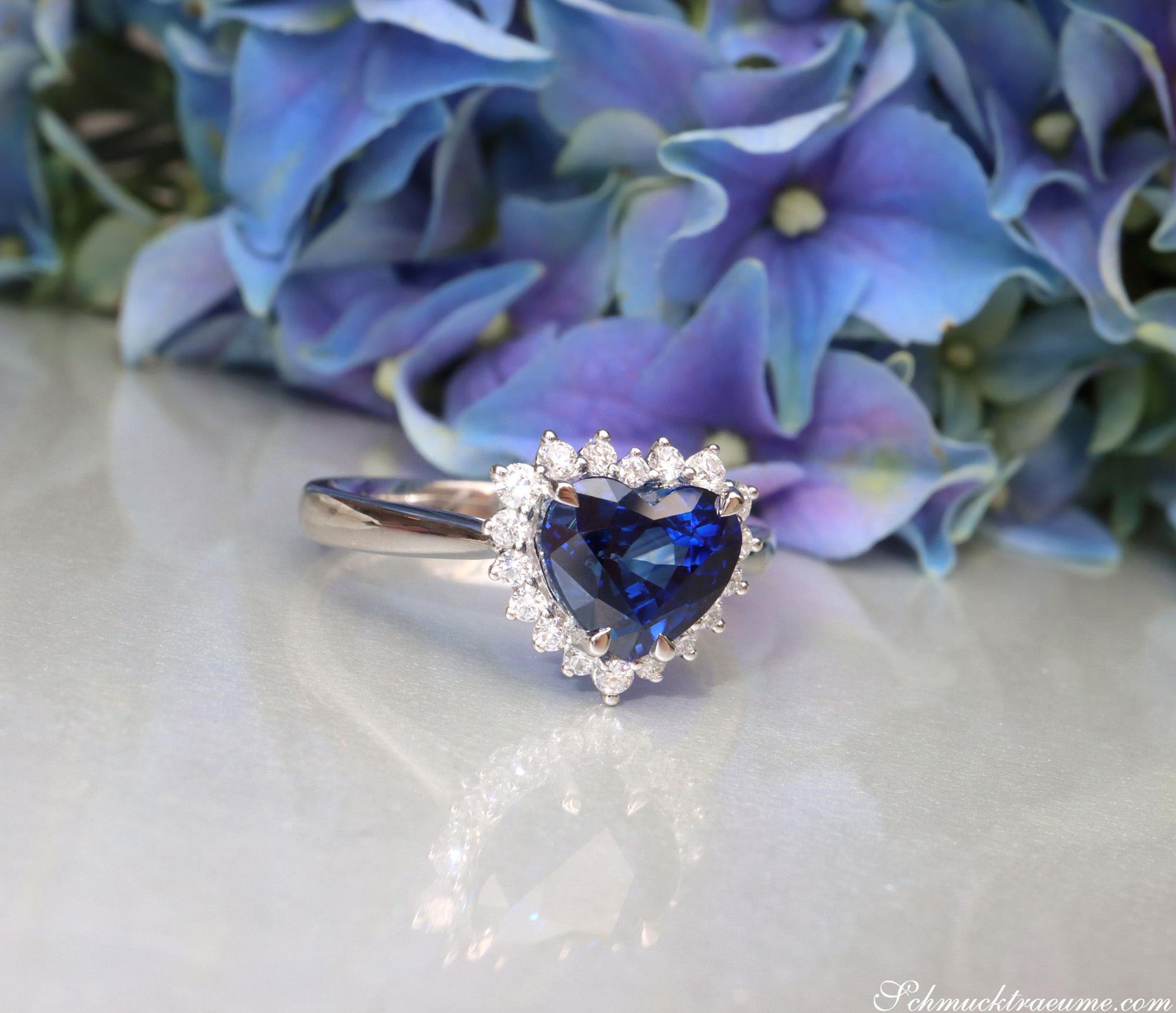 Herzformiger Saphir-Ring mit Brillanten, Detailaufnahme auf Blumenhintergrund.