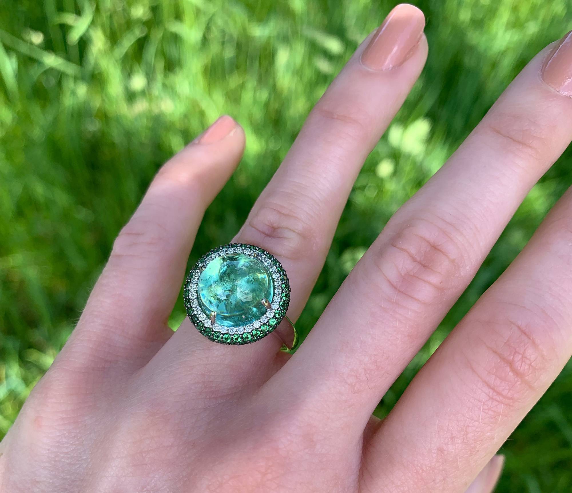 Mintfarbener Turmalin-Ring mit Tsavorite und Brillanten, auf grünem Hintergrund getragen.