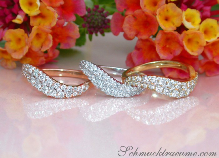 Blumig präsentiert: Drei geschwungene Brillantenringe in Goldfarben auf Blütenhintergrund