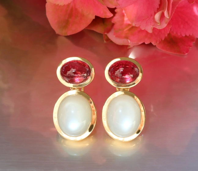 Rubellit und Mondstein Ohrringe in Gelbgold, elegant auf glänzender Oberfläche Rubellit und Mondstein Ohrringe in Gelbgold, elegant auf glänzender Oberfläche