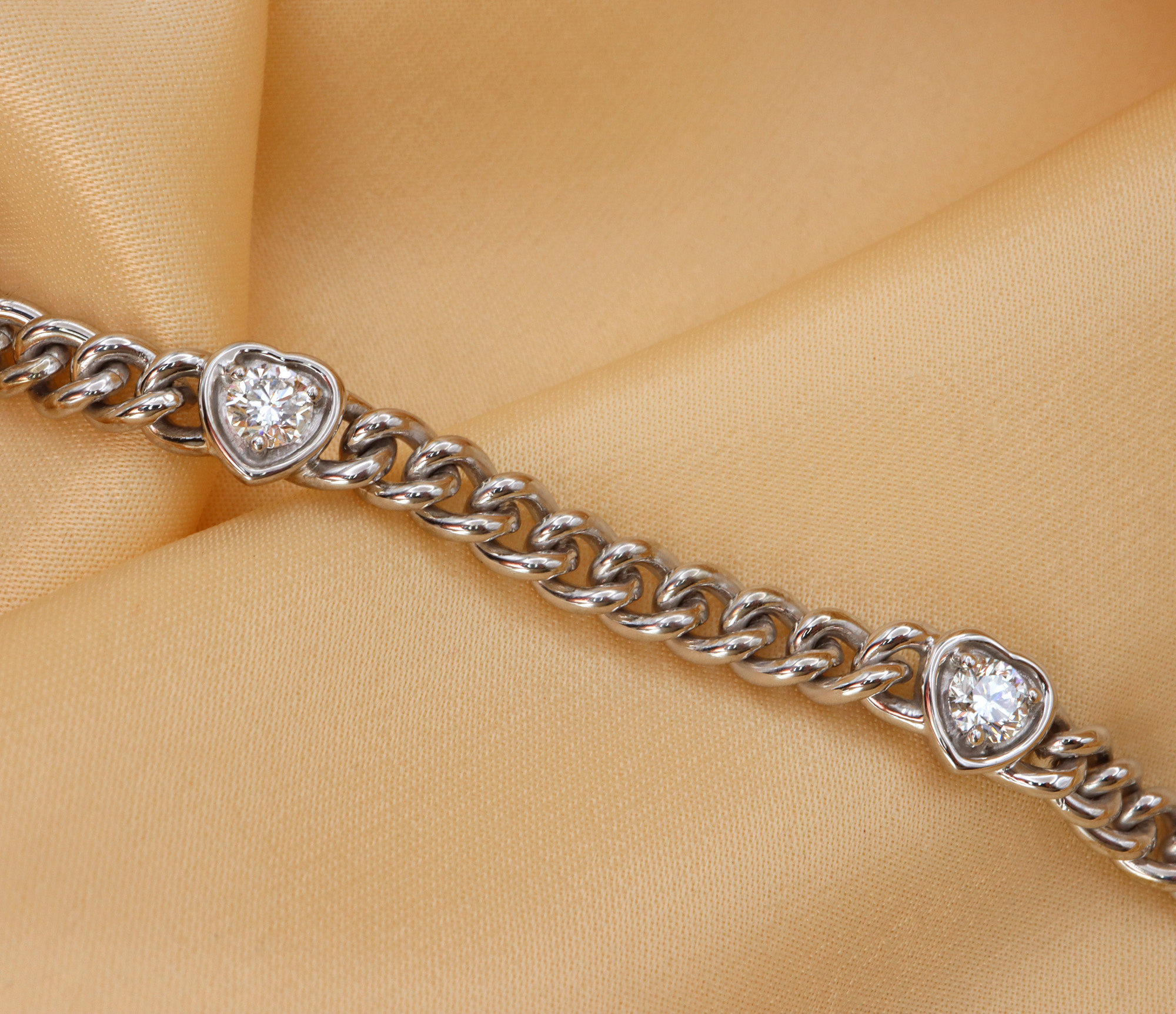 Weiße Panzerarmband mit Brillantenherzen auf cremefarbenem Stoff, Detailaufnahme.