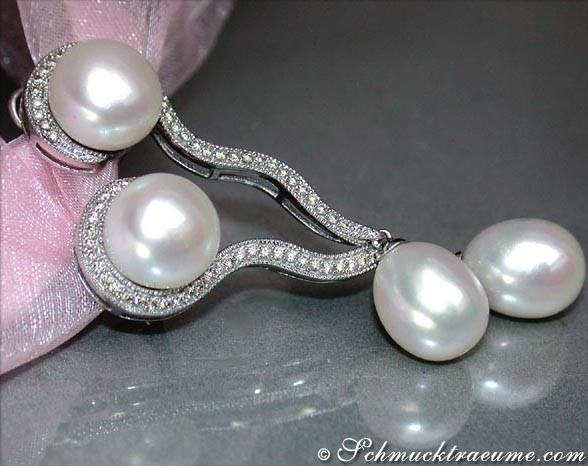 Geschwungene Süßwasserperlen-Ohrhänger mit Brillanten, detailreich, elegant, vor rosa Schleife.