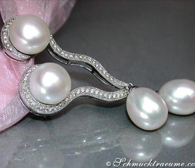 Geschwungene Süßwasserperlen-Ohrhänger mit Brillanten, detailreich, elegant, vor rosa Schleife. Geschwungene Süßwasserperlen-Ohrhänger mit Brillanten, detailreich, elegant, vor rosa Schleife.