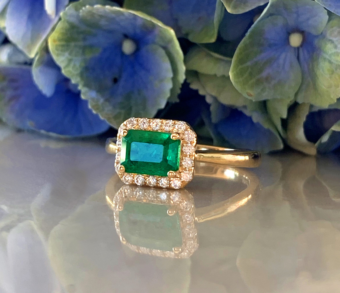 Smaragd-Ring mit Brillanten in Gelbgold 585, detailreich, blau-grüne Blüten im Hintergrund.