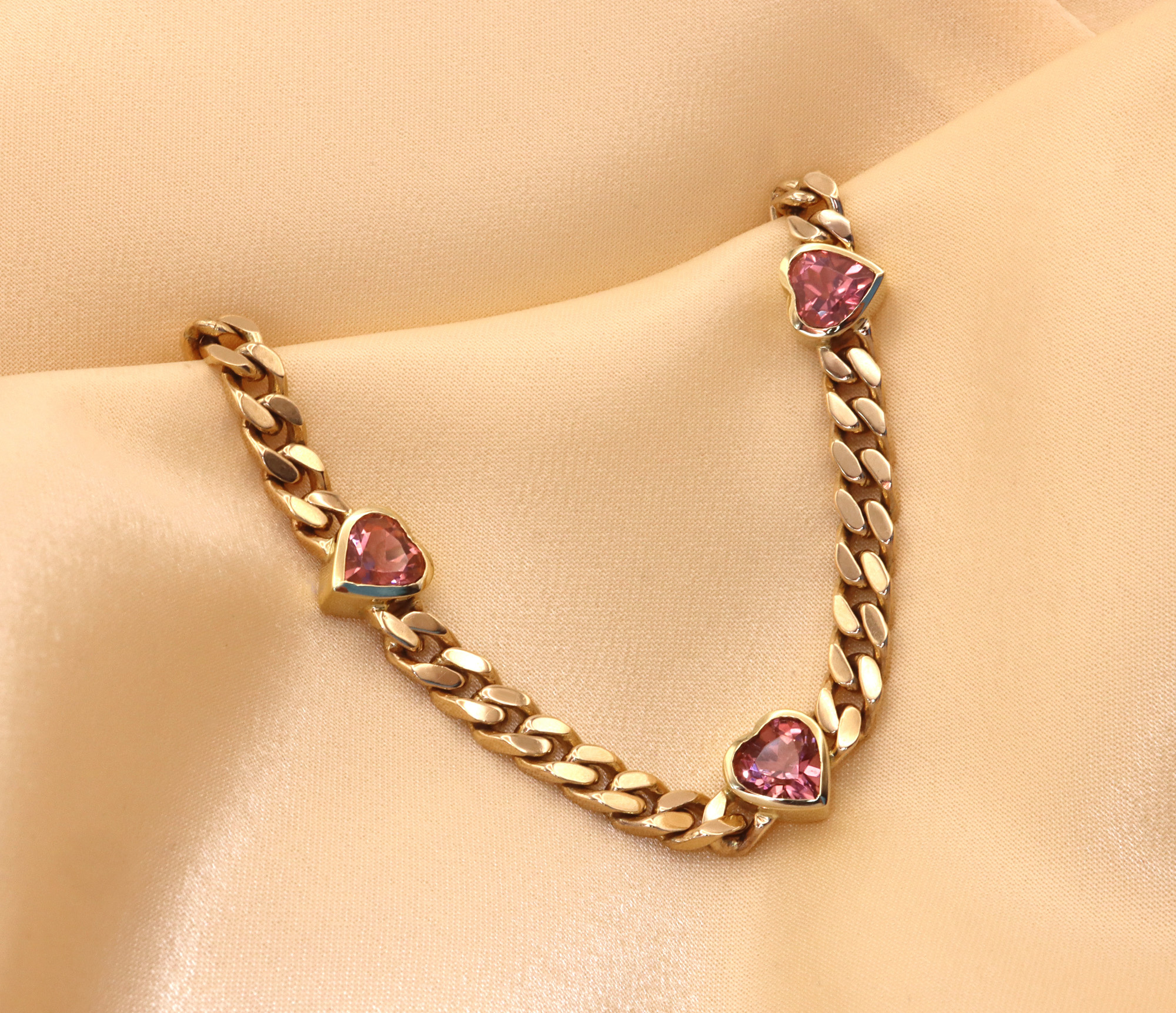 Goldene Panzerarmband mit rosa Turmalin-Herzen auf cremefarbenem Stoff