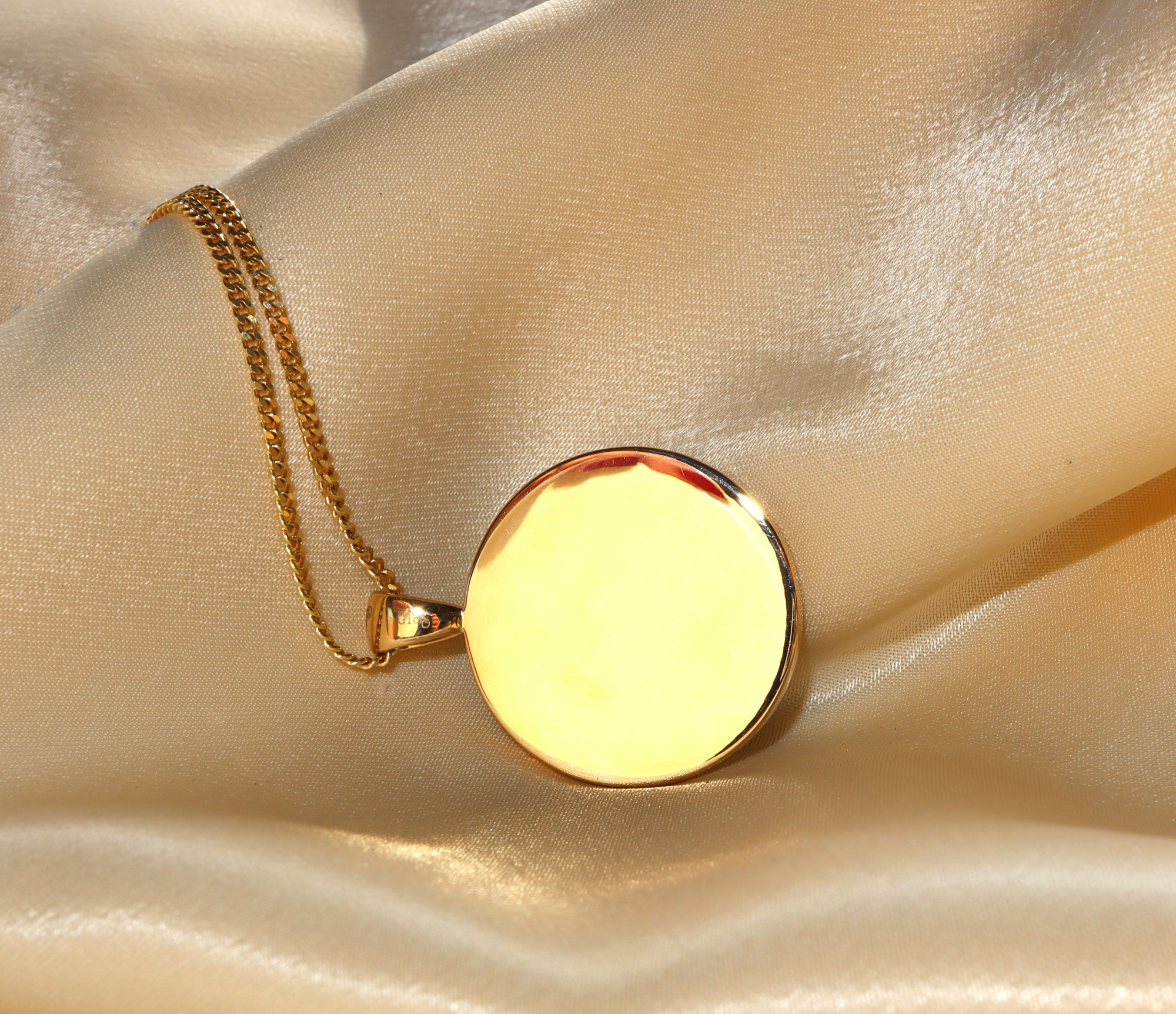 Goldene Kette mit runder Malachitanhänger auf Seidenstoff, Detailaufnahme