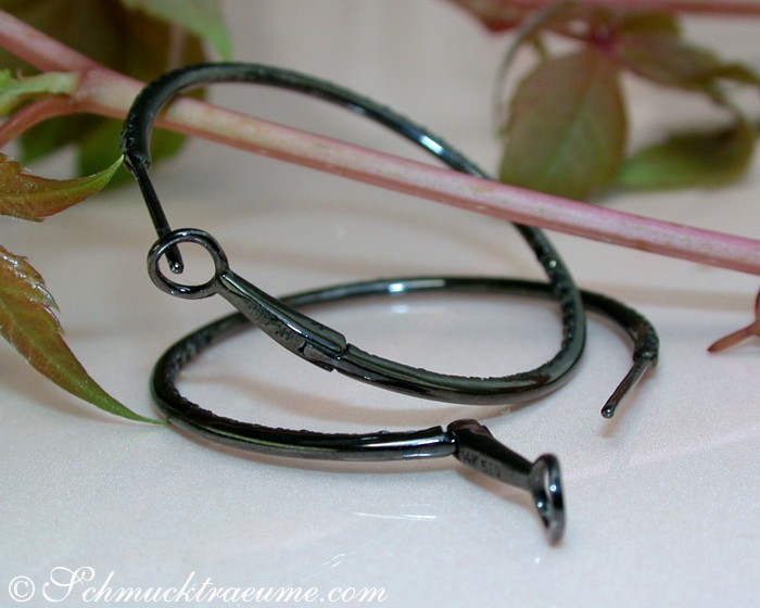 Schwarze Creolen aus Weißgold mit Diamanten, Detailaufnahme, zarte Form, grüne Pflanzen im Hintergrund