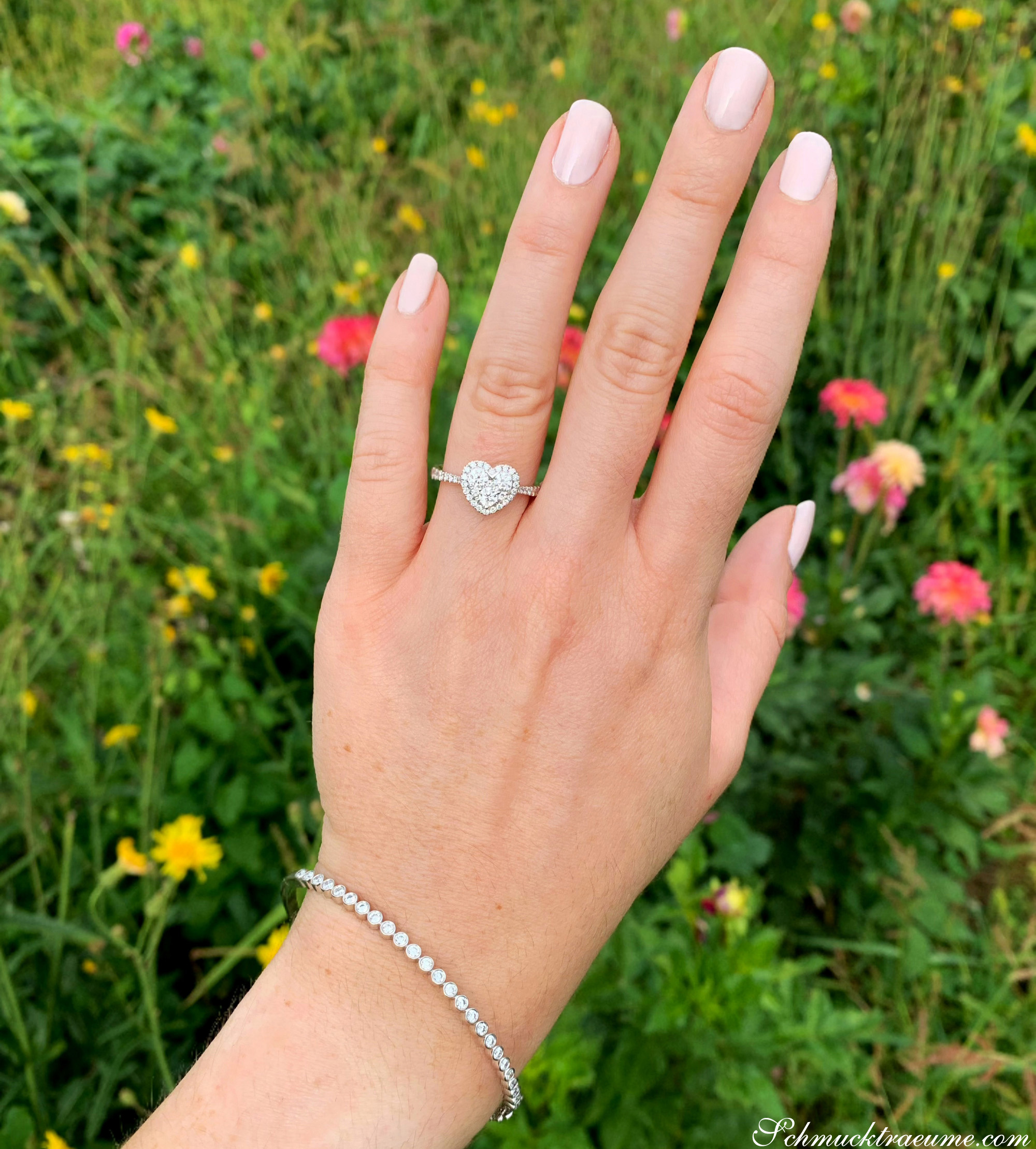 Weißgold Herzring mit Brillanten, getragen im Freien mit Blumen im Hintergrund