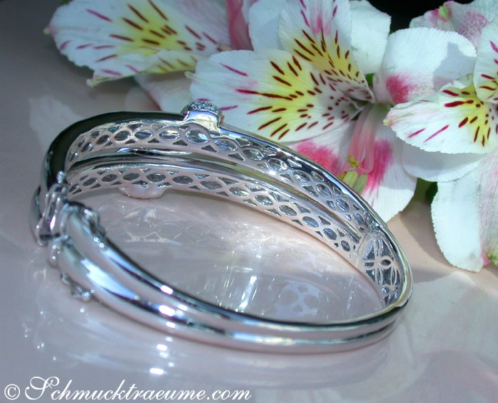 Silberner Armreif mit Lattendesign auf weißem Untergrund, Blüten im Hintergrund