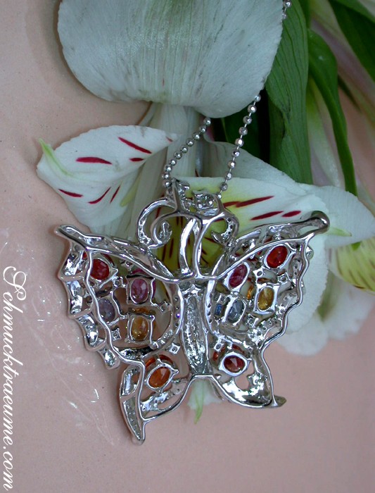 Edelstein-Schmetterling-Anhänger mit Regenbogen-Saphiren und Brillanten, Detailaufnahme auf weißem Blütenhintergrund.