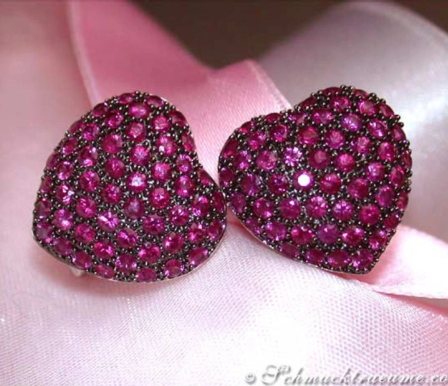 Herzformige Ohrstecker aus Weißgold 585 mit 3.750 Rubinen, auf rosa Seide liegend. Herzformige Ohrstecker aus Weißgold 585 mit 3.750 Rubinen, auf rosa Seide liegend.