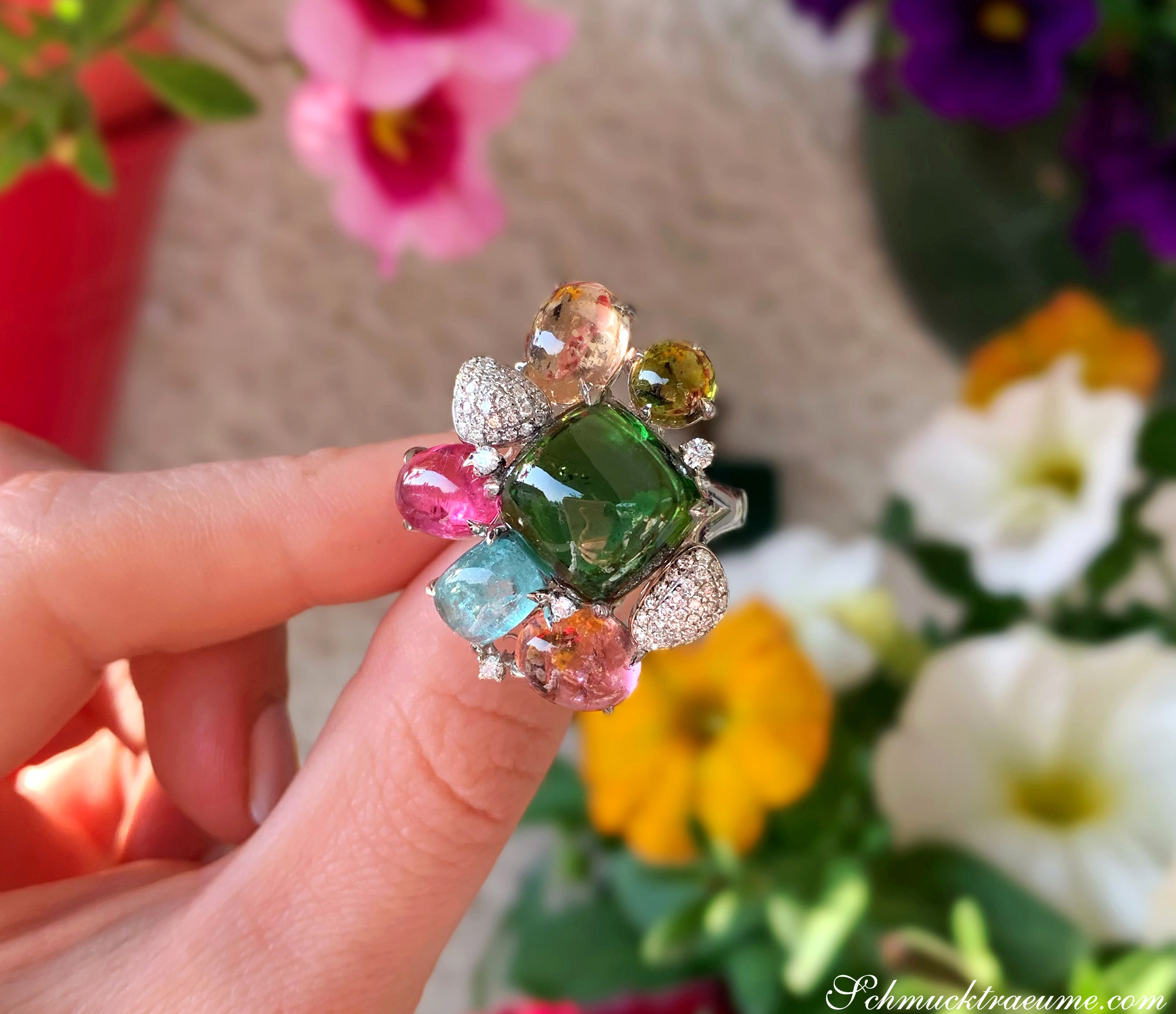 Weißgold-Ring mit farbenfrohen Turmalinen und Brillanten, Detailaufnahme, im Hintergrund Blumen.