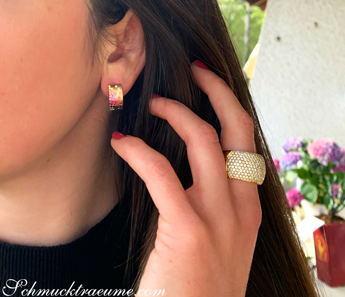 Edle Multicolor Saphir Sternenhimmel Ohrringe: Frau mit roten Nägeln, Ring am Finger, Hintergrund mit Blumen.