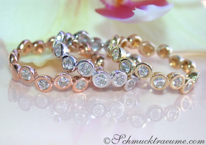 Detailansicht von drei Brillantenringen in Weiß-, Gelb- und Roségold, funkelnd auf glattem Hintergrund.