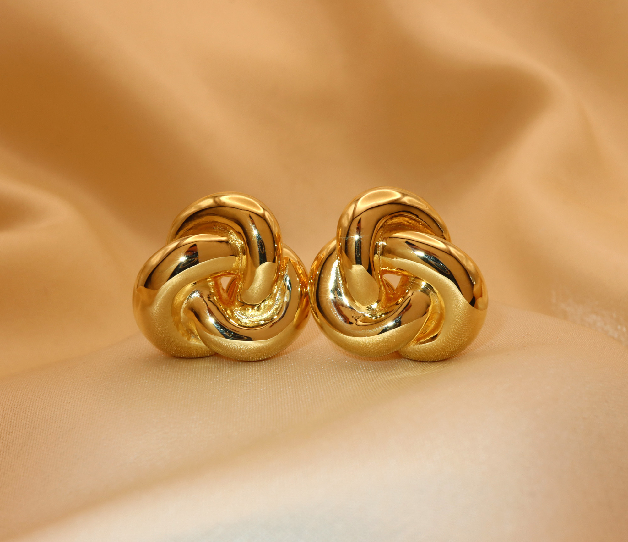 Goldene Knoten-Ohrstecker aus 585er Gelbgold, Detailansicht auf cremefarbener Stoffoberfläche