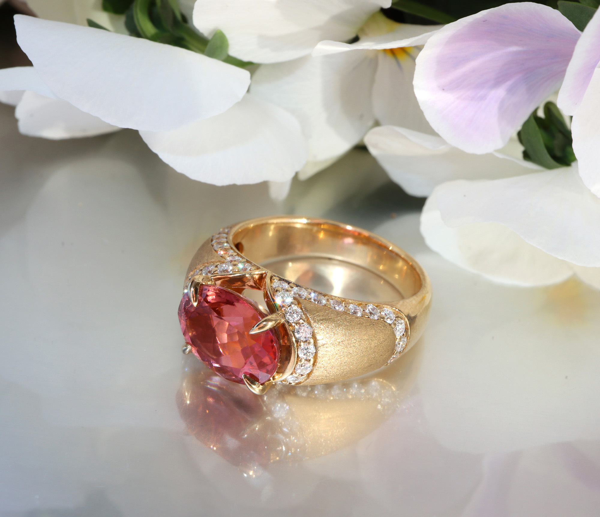 Goldener Ring mit rosa Turmalin und Diamanten, auf Blumen liegt.