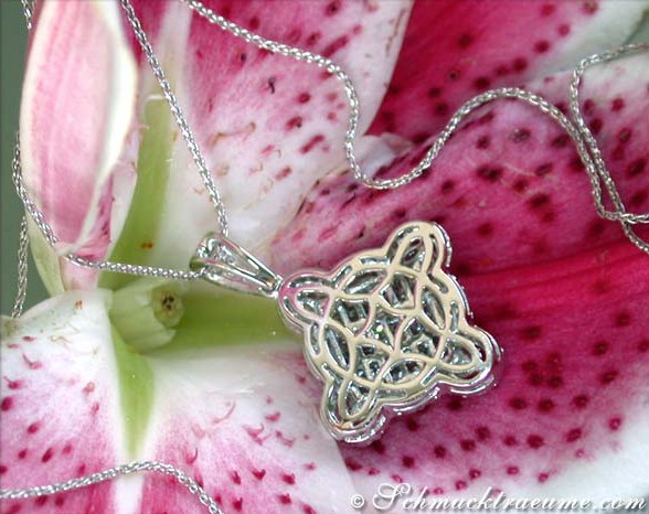 Silberner Anhänger mit filigranem Diamantenschliff, hängend an einer Kette, vor Lilie.