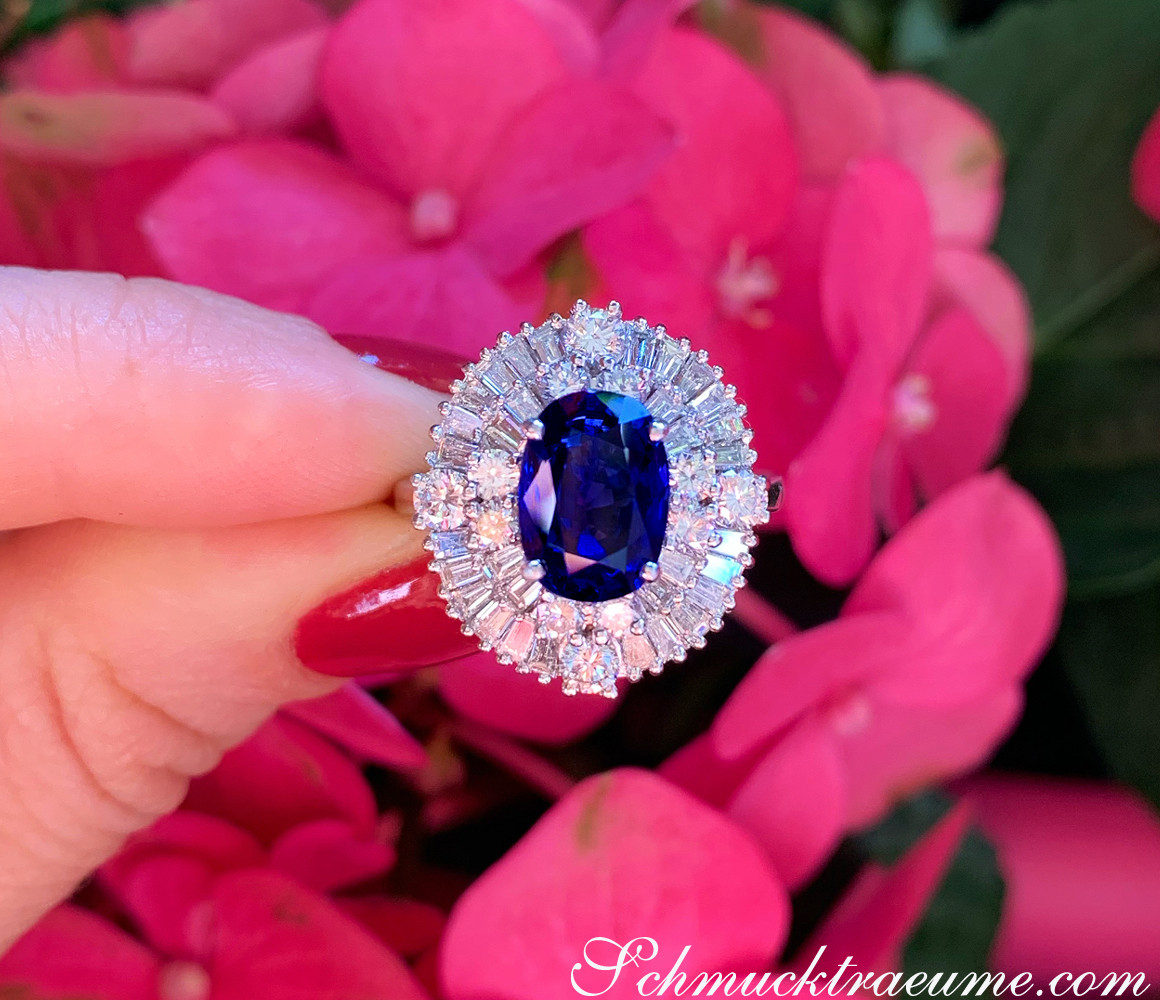 Ringszene: Hand hält prächtigen Saphirring mit Diamanten vor rosa Blüten