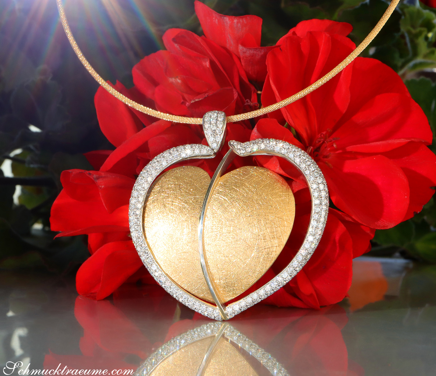 Goldener Herz-Anhänger mit Brillanten, Detailaufnahme, vor roten Blüten.