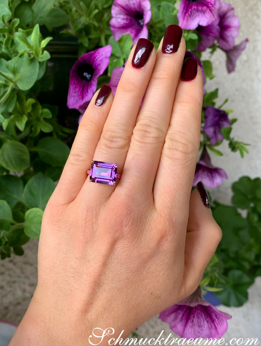Amethyst-Ring mit Rubinen auf Hand vor Blumen, Detailaufnahme