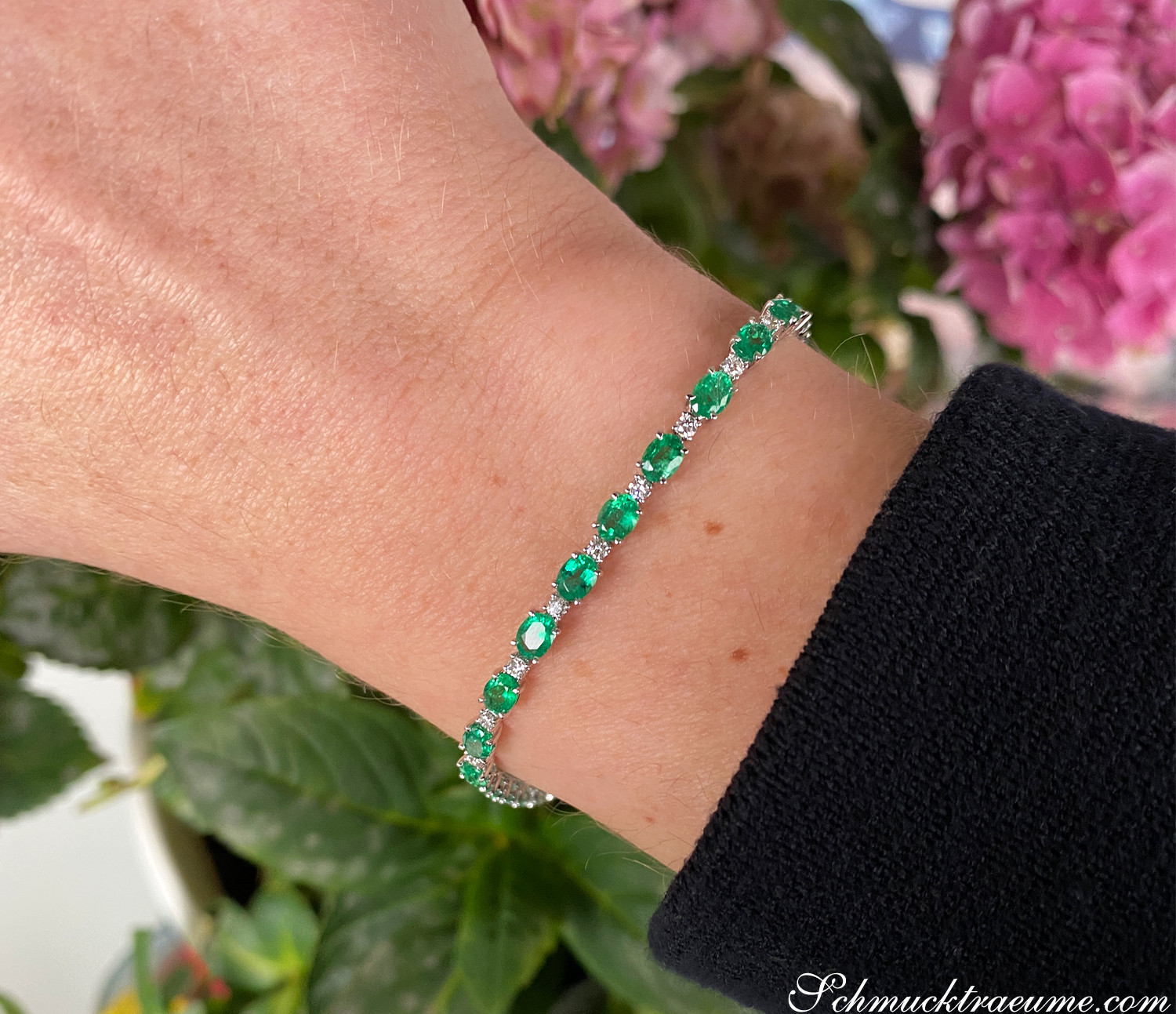 Smaragd-Armband mit Brillanten auf Hand mit Blumen im Hintergrund