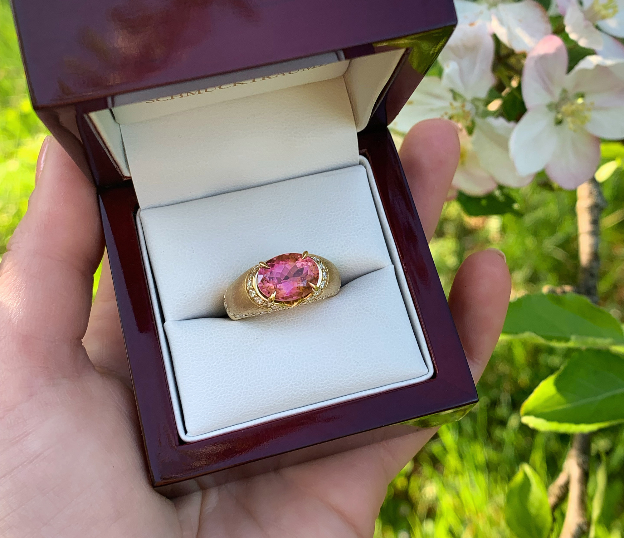 Rosa Turmalin Brillanten-Ring in Gelbgold, im Freien mit Blüten im Hintergrund