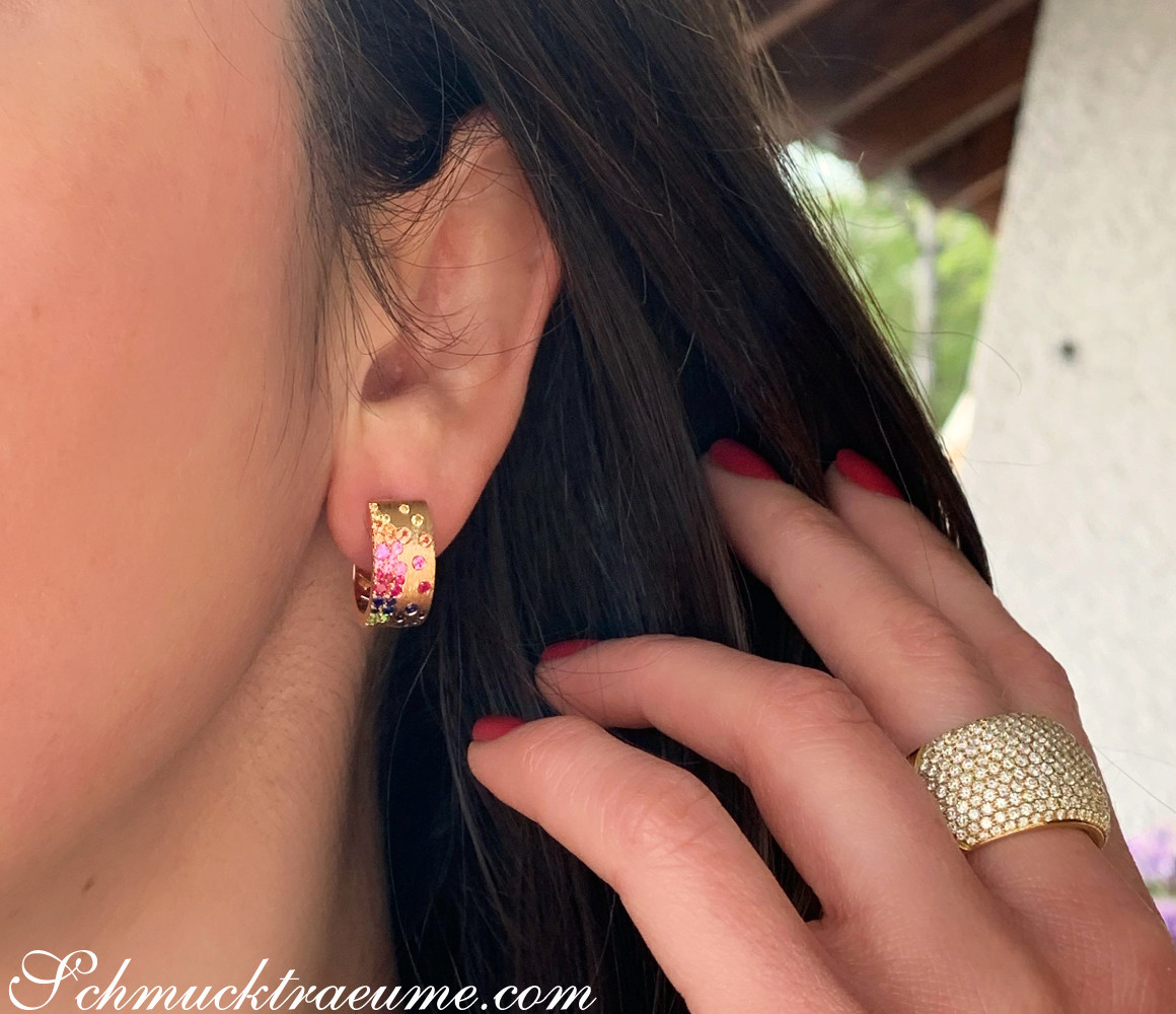 Detailansicht von Multicolor-Saphir-Ohrhänger in Gelbgold, Frau mit roten Nägeln, Haar im Vordergrund.