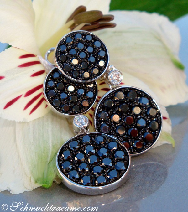 Schwarze Diamant-Ohrgehänge mit Brillanten, Detailaufnahme, weißer Blüte im Hintergrund