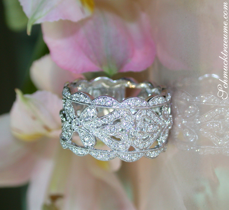 Detail des Diamant-Rings im Antik-Design, getragen auf zartem Stoff, mit floraler Blume im Hintergrund