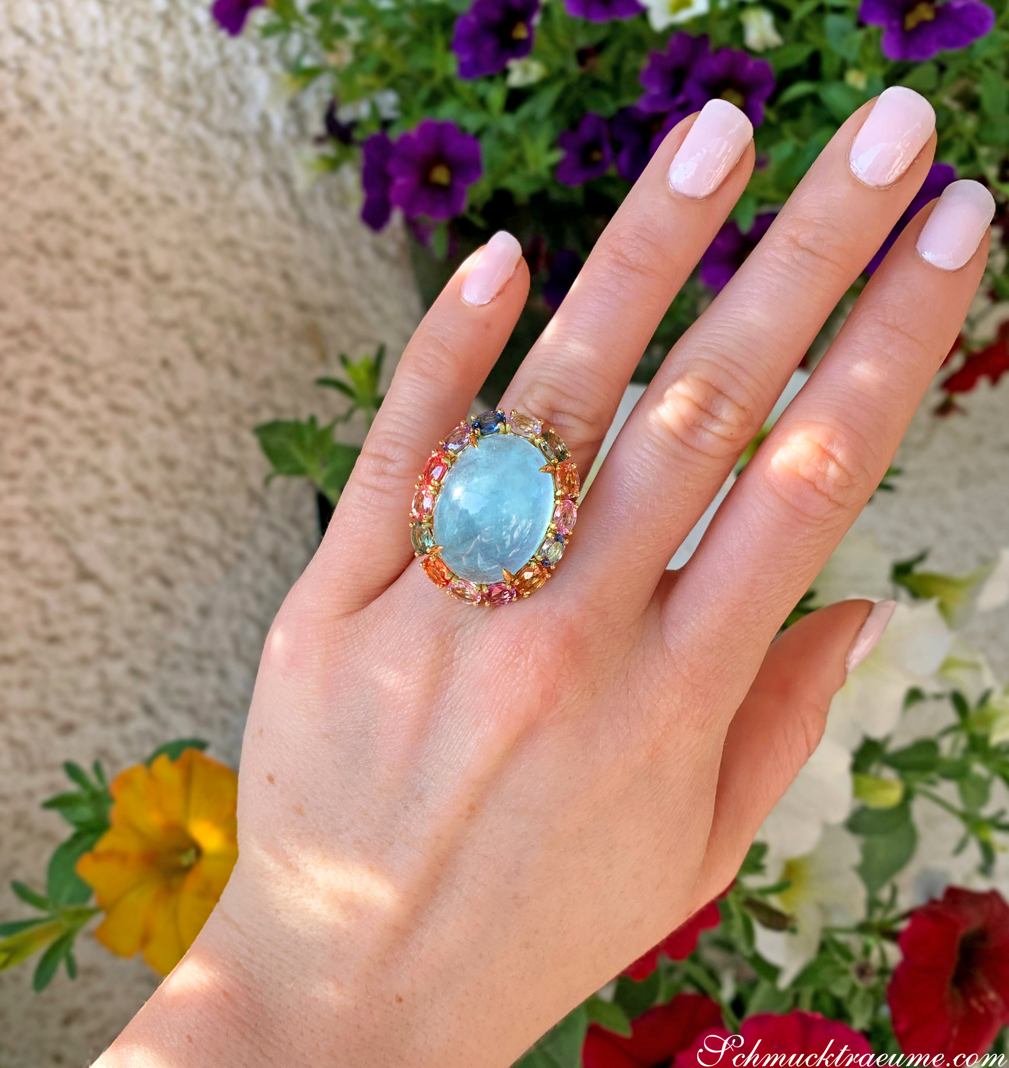 Opulenter Milky Aquamarin-Ring mit Multicolor Saphiren auf Hand vor Blumen