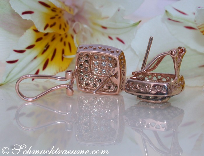 Roségold-Ohrringe mit Brillanten auf Blütenhintergrund