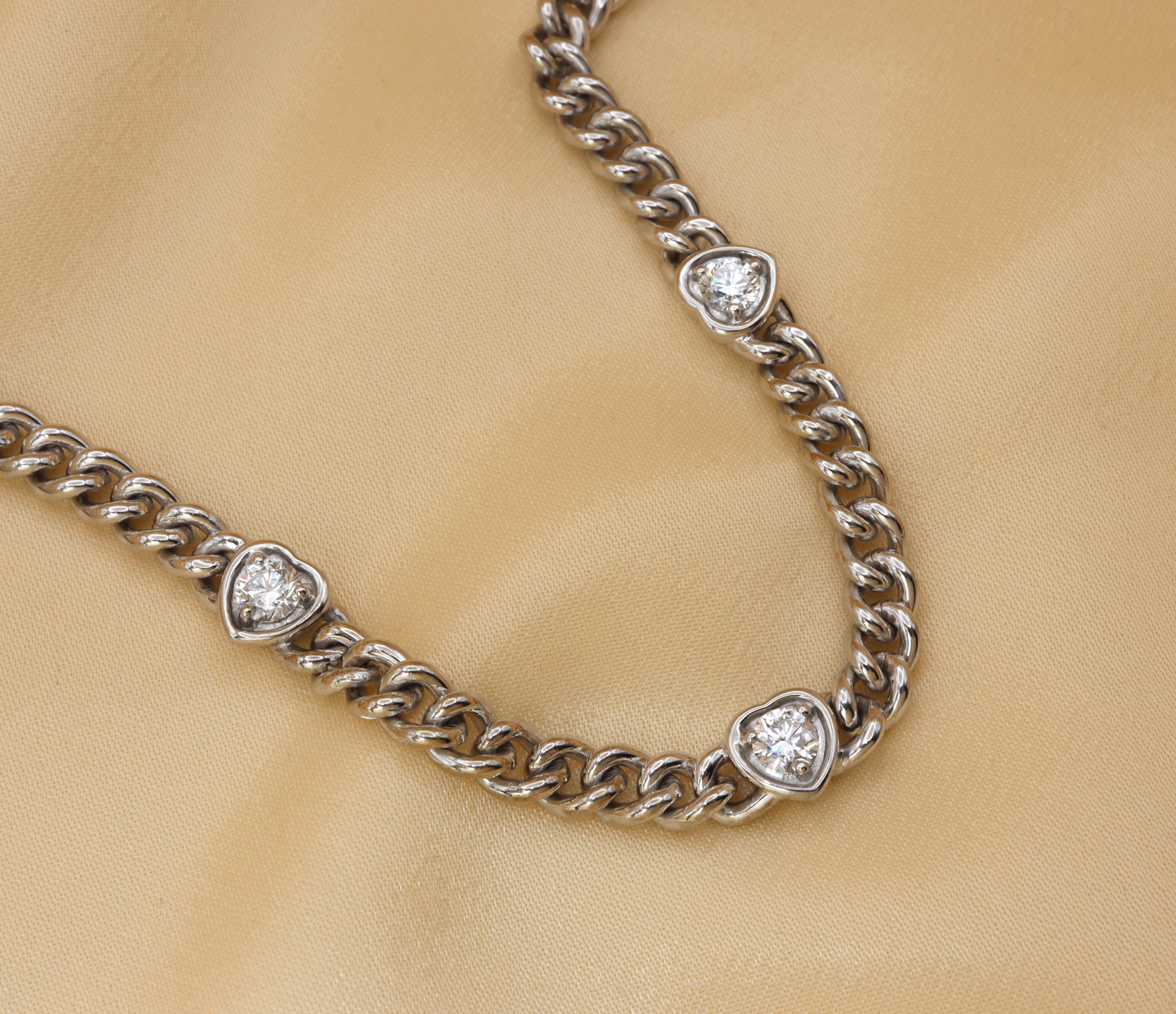 Silbernes Panzerarmband mit Diamantherzen auf glänzender Seide