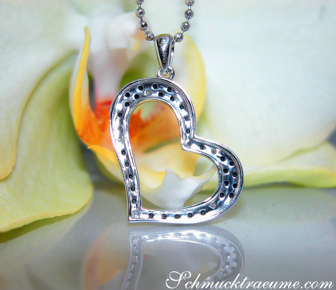 Silberner Herzanhänger mit schwarzen Diamanten, dezent und elegant, vor Orchideenblüte.