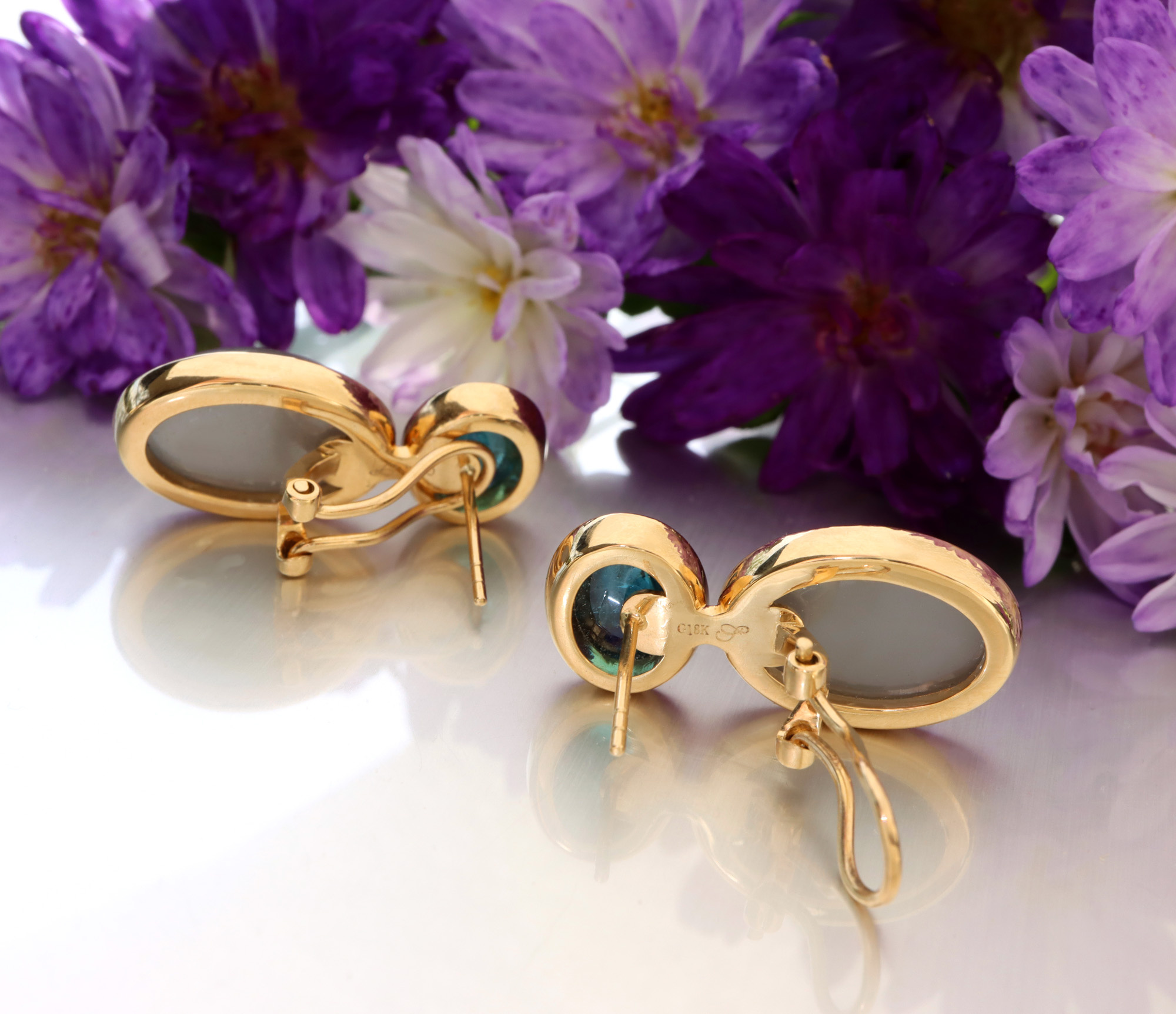 Goldene Ohrringe mit Mondsteinen, blühende Blumen im Hintergrund