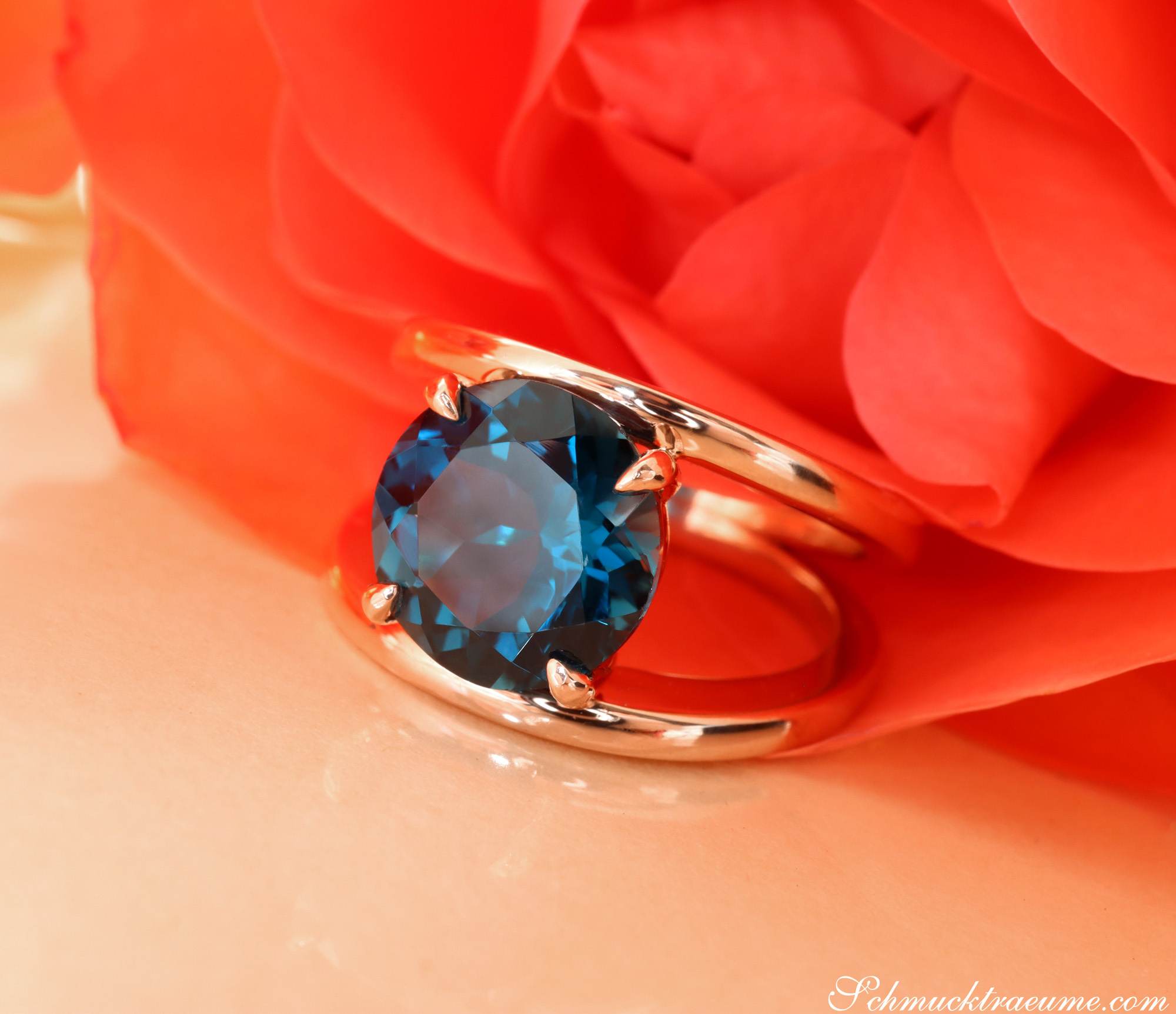 Blautopas-Ring aus 585er Roségold mit rundem Schliff vor Rosenblüte