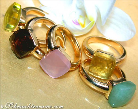 Goldene Ringe mit farbenfrohen Steinen, Orchideen im Hintergrund