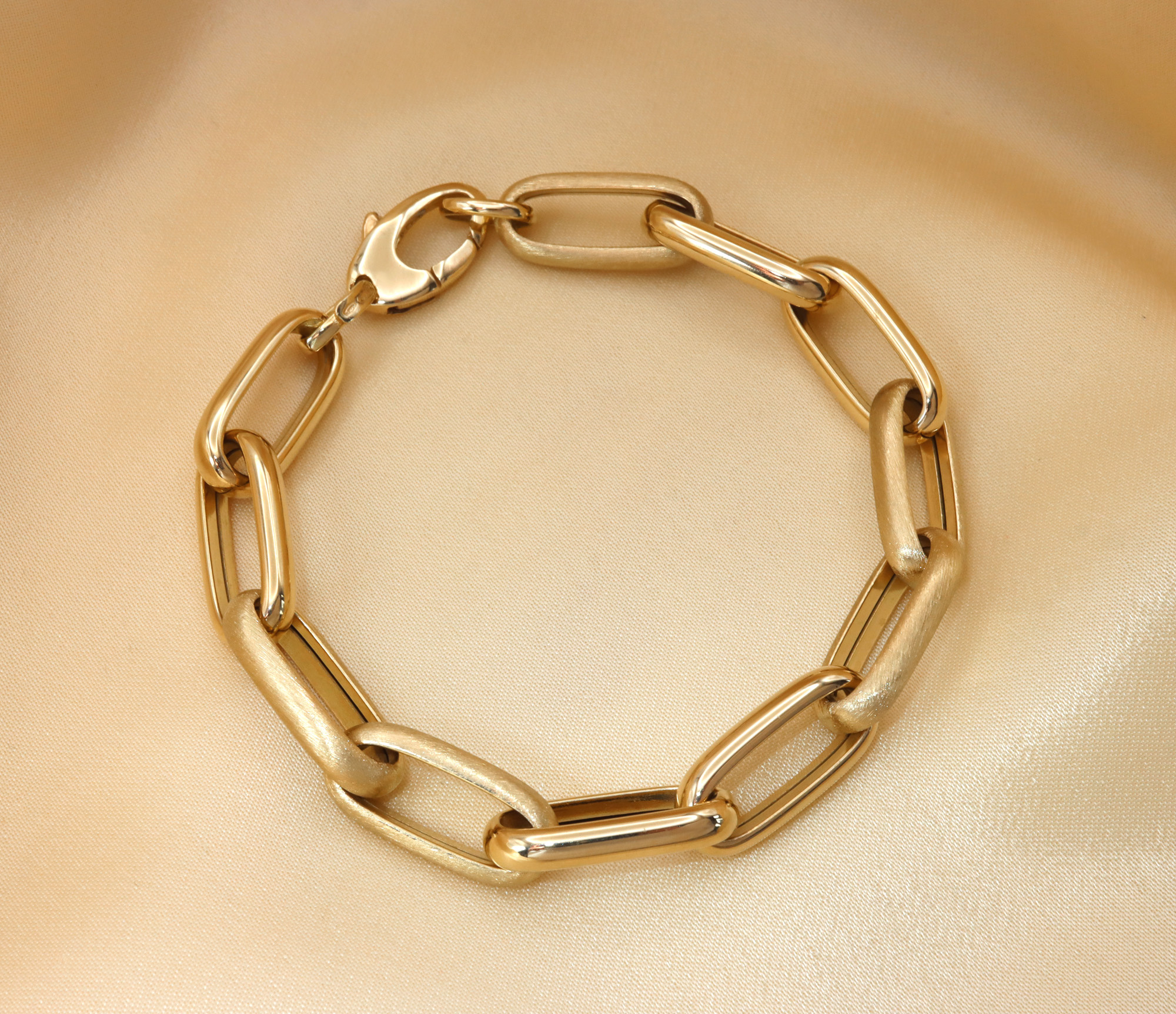 Goldenes Paperclip-Armband aus 585er Gelbgold, glänzend und satiniert, auf cremefarbenem Stoff liegend.