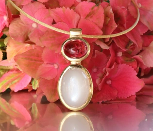 Goldene Halskette mit Rubellit und Mondstein, vor rosa Blütenblättern.