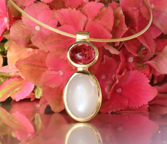 Goldene Halskette mit Rubellit und Mondstein, vor rosa Blütenblättern. Goldene Halskette mit Rubellit und Mondstein, vor rosa Blütenblättern.