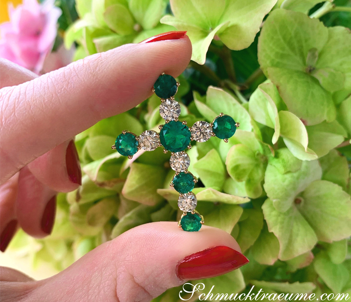 Gelbgold Kreuzanhänger mit Smaragden und Brillanten, Detailaufnahme auf grünen Blättern.