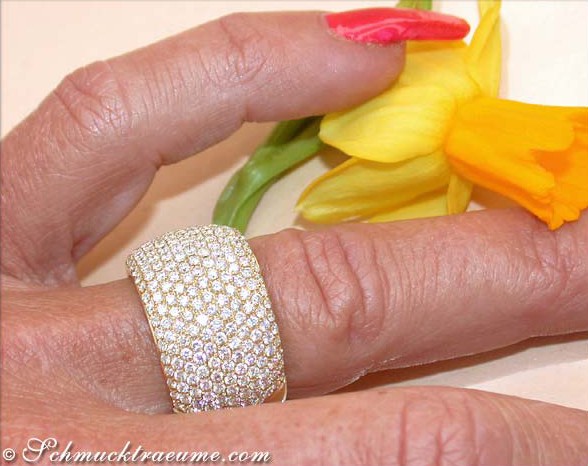 Goldener Brillanten-Pavé-Ring auf Hand mit gelber Blume im Hintergrund
