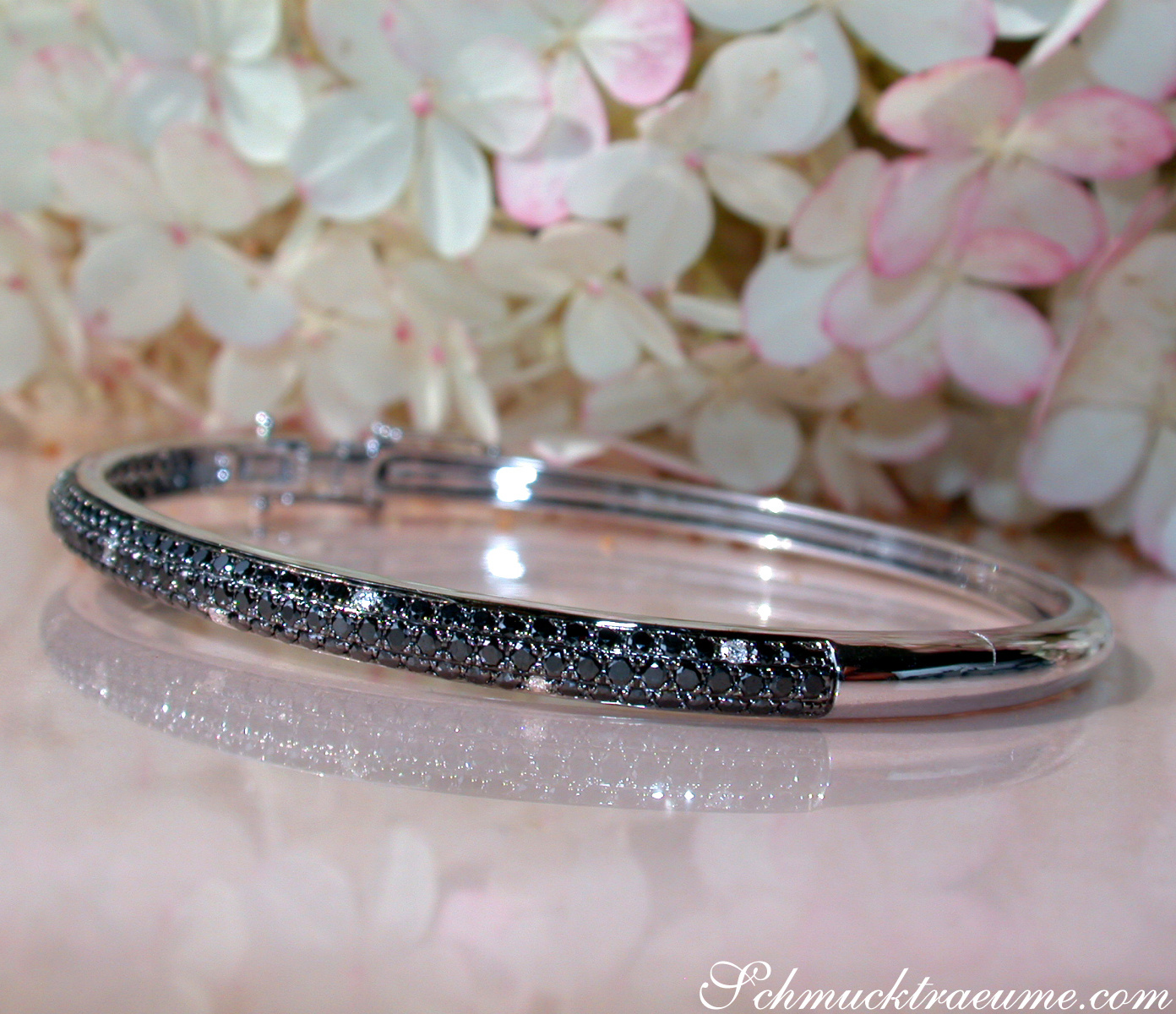 Weißgold-Armreif mit schwarzen Diamanten, Detailaufnahme, Blumen im Hintergrund.