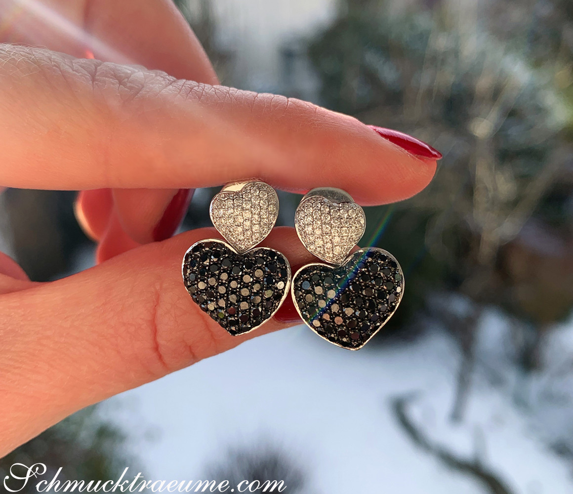 Weißgold-Ohrstecker mit Diamantenherzen, Detailaufnahme, Hand mit rotem Nagellack, verschneiter Hintergrund.