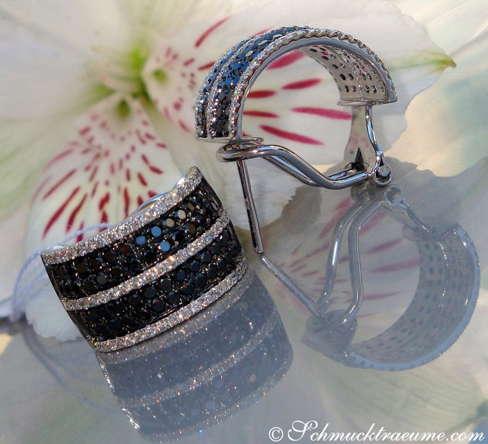 Schwarzgoldene Halbcreolen mit schwarz-weißen Diamanten, Detailaufnahme, elegant auf Blüte präsentiert