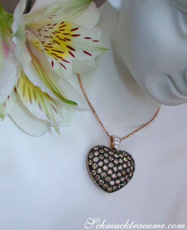 Weißgold-Herz-Anhänger mit braunen Brillanten, detailreich, auf weißem Hintergrund, neben Blume.