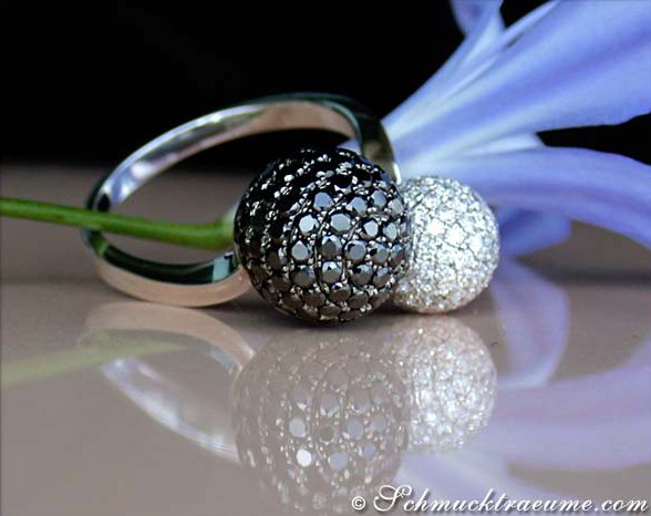 Schwarz-weißer Pavé-Kugel-Ring mit Diamanten, Detailaufnahme, blauer Blume im Hintergrund