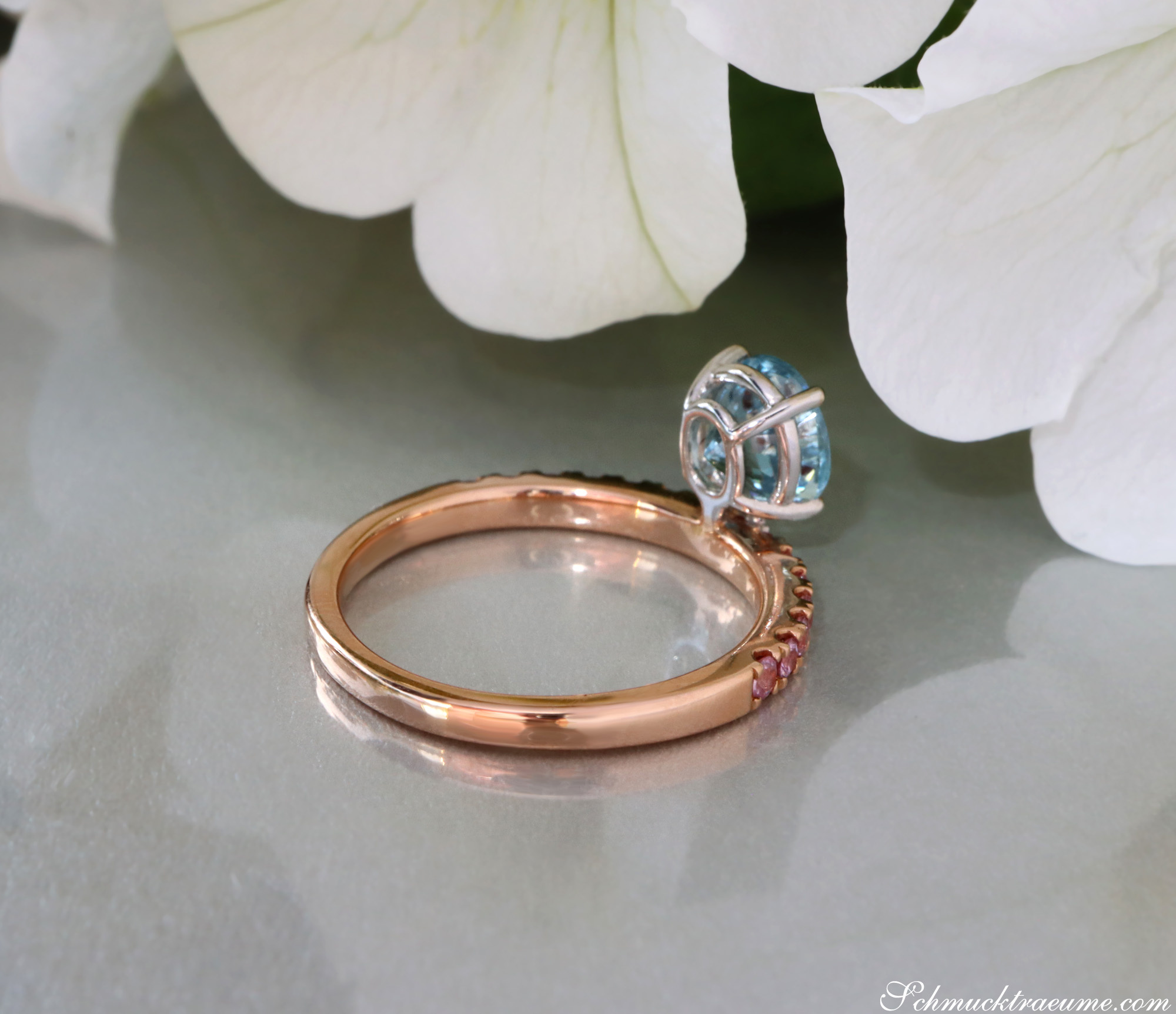 Raffiniertes Aquamarin-Ring mit rosa Saphiren, detailreiches Design, weißer Hintergrund, Blume im Hintergrund.