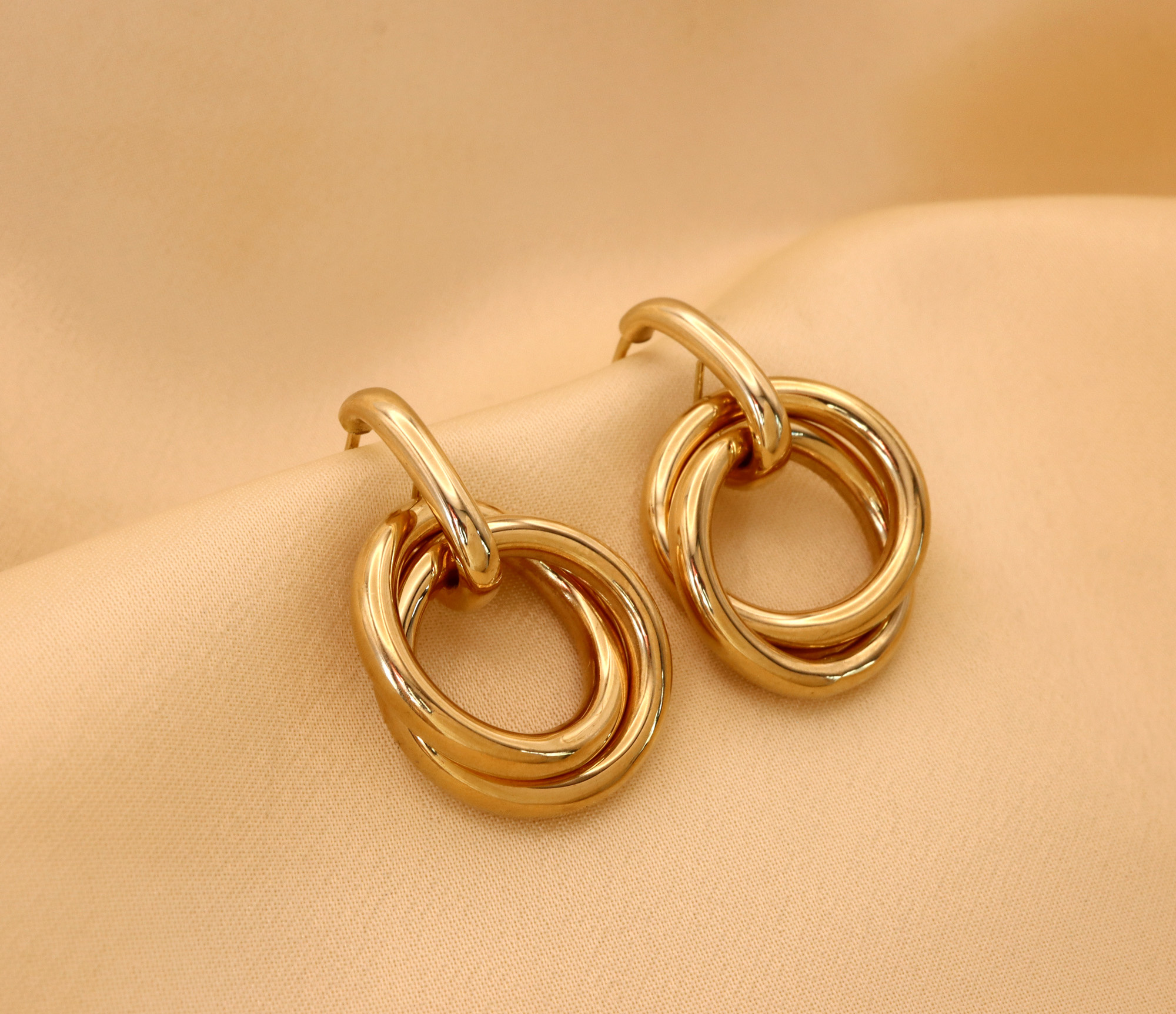 Goldene Ohrringe aus 585er Gelbgold, geschwungen, glänzend, auf cremefarbener Oberfläche liegend.