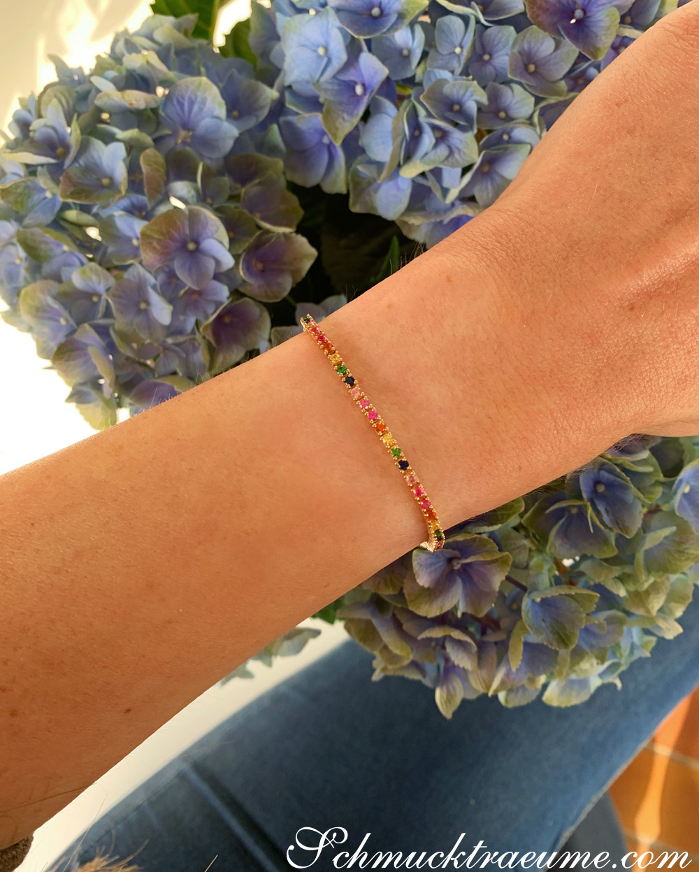 Armband mit farbenfrohen Saphiren auf der Hand vor blauen Hortensienblüten