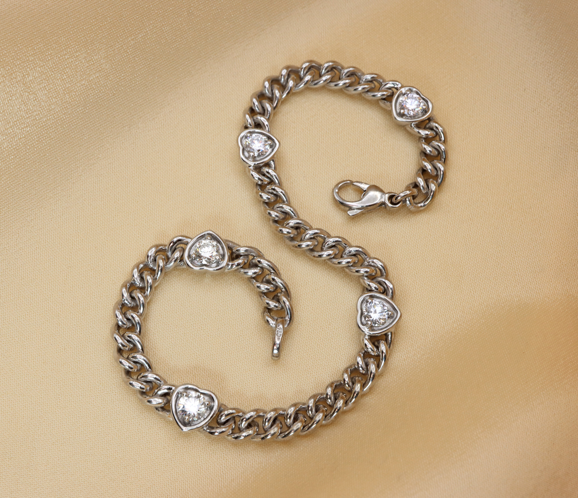 Glänzende Panzerarmband mit Brillantenherzen, Detailaufnahme auf cremefarbenem Hintergrund